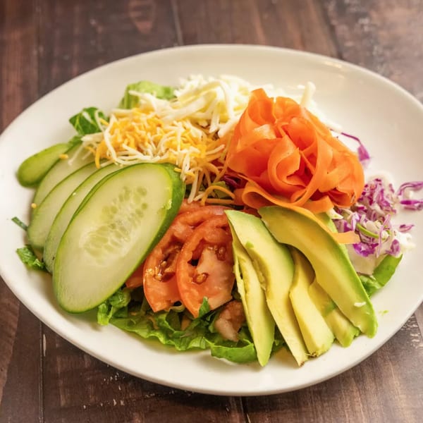 A vibrant salad with lettuce, cucumbers, tomatoes, avocado, shredded carrots, and cheese on a white plate.