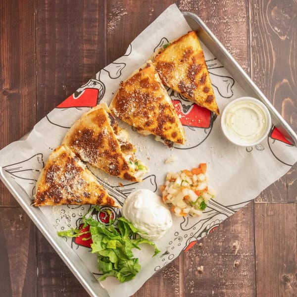 Four quesadilla slices with sour cream, salsa, and lettuce on a metal tray with parchment paper.