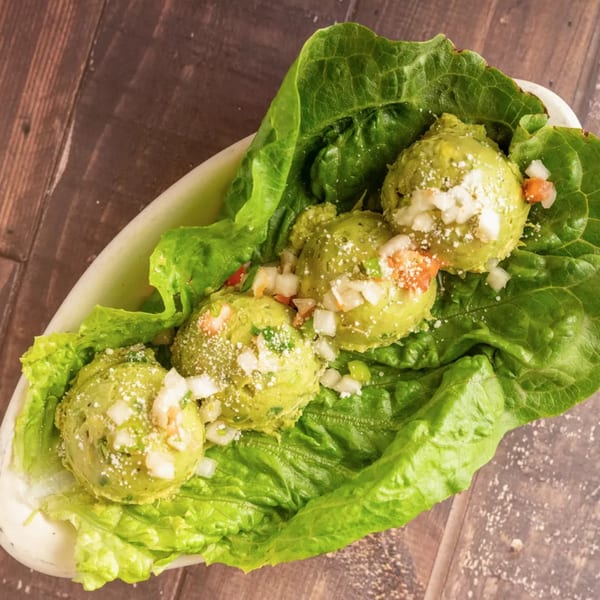 Four scoops of guacamole with diced onions, tomatoes, and cheese, served on lettuce leaves.