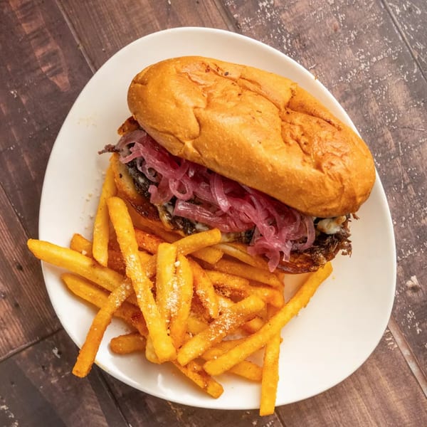 A delicious cheesesteak sandwich with pickled red onions and a side of golden french fries.
